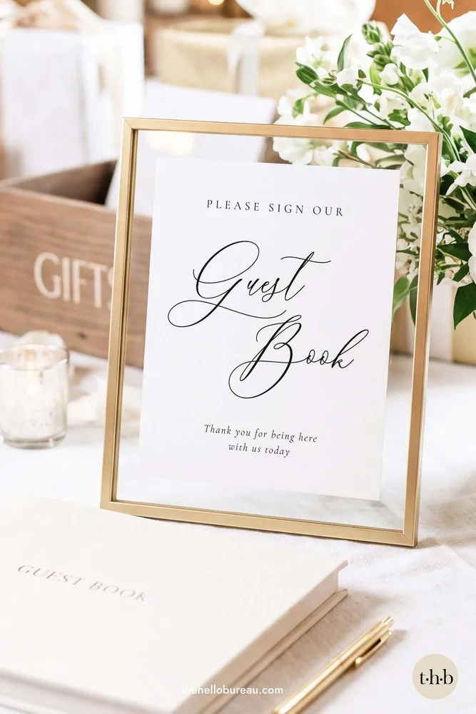 Classic and formal please sign our guestbook sign in a gold frame beside white flowers and a cream guestbook