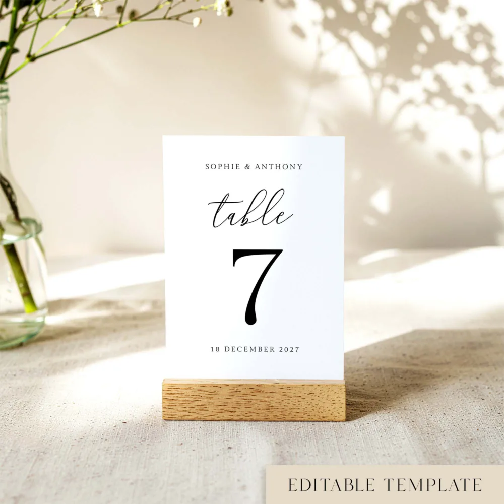 Modern minimalist wedding table number template featuring "Table 7" with chic script calligraphy and the couple's names. Marais design shown in a wooden base. No software required to edit this high-end look.