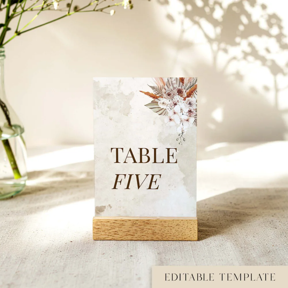 Boho wedding table number template featuring "Table Five" in serif typography with earthy watercolour florals and pampas grass. Shown in a timber stand. Personalise this Solana design in your browser at The Hello Bureau.