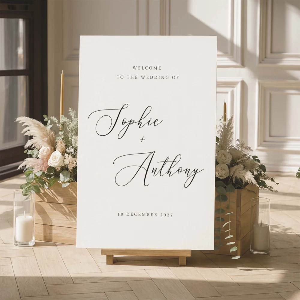 Elegant wedding entry sign with sophisticated calligraphy and minimalist serif accents. The Marais template is shown in a bright indoor studio with pampas grass and candles, offering a timeless editorial look for modern couples.