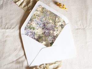 White envelope with a printed liner showing painted small purple and white flowers.