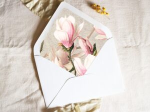 White envelope with a printed liner showing painted pink magnolias on a grey background.