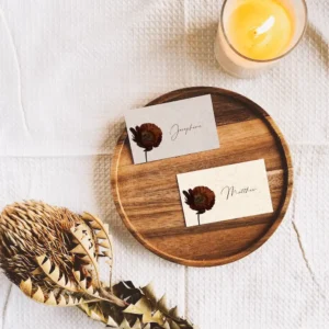 Two place cards sitting on a plate next to a candle and dried flower