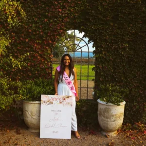 A woman standing in a garden next to a welcome sign