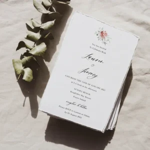 A stack of wedding invitations on a table next to eucalyptus