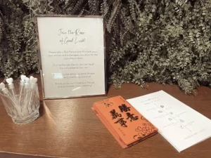 A small sign in a frame on a wooden table next to Chinese red packets