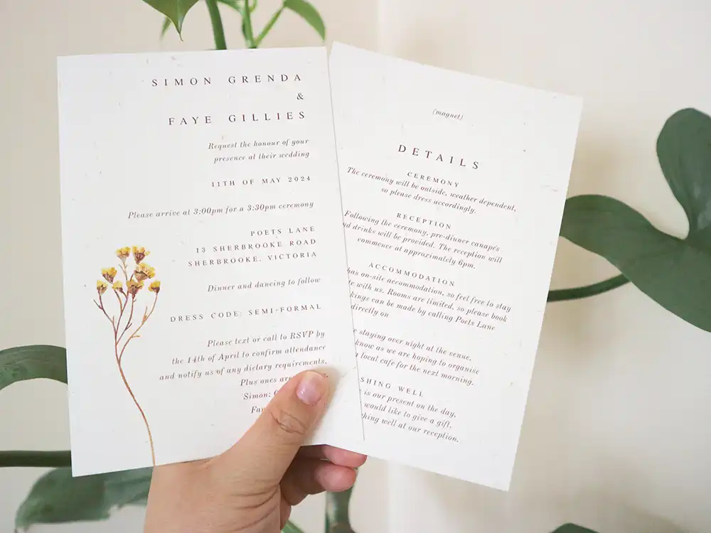 A hand holding double-sided wedding invitations