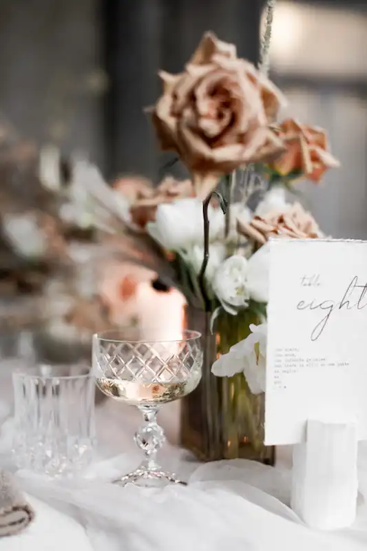 A wedding table setting with glassware, roses and printed table number