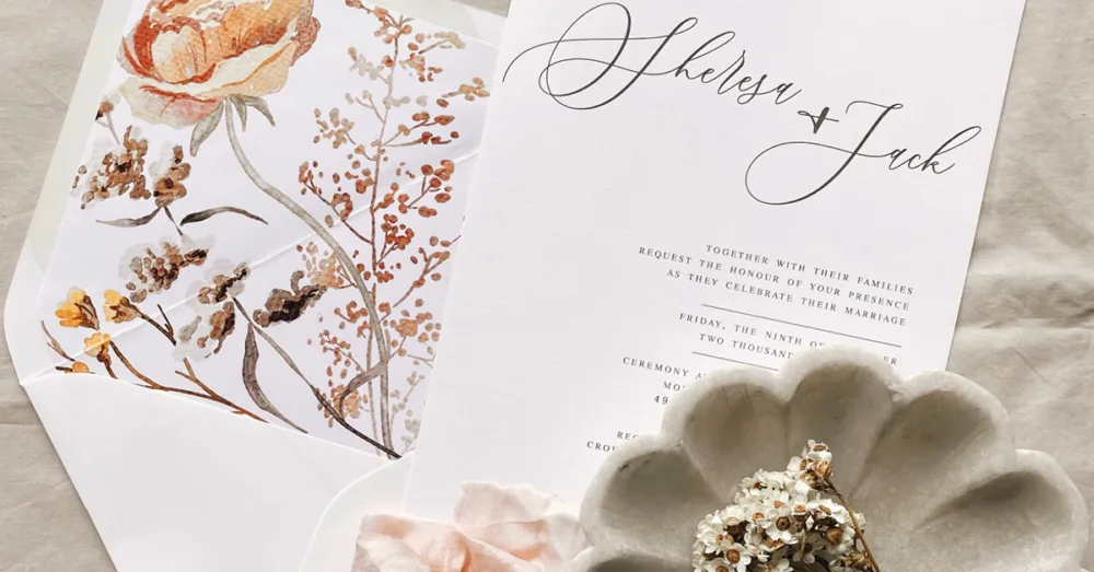 An elegant wedding invitation next to an open envelope with floral liner.