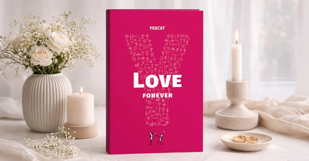 YOUCAT Love Forever Book sitting on a table with wedding rings, candles and a vase of flowers.