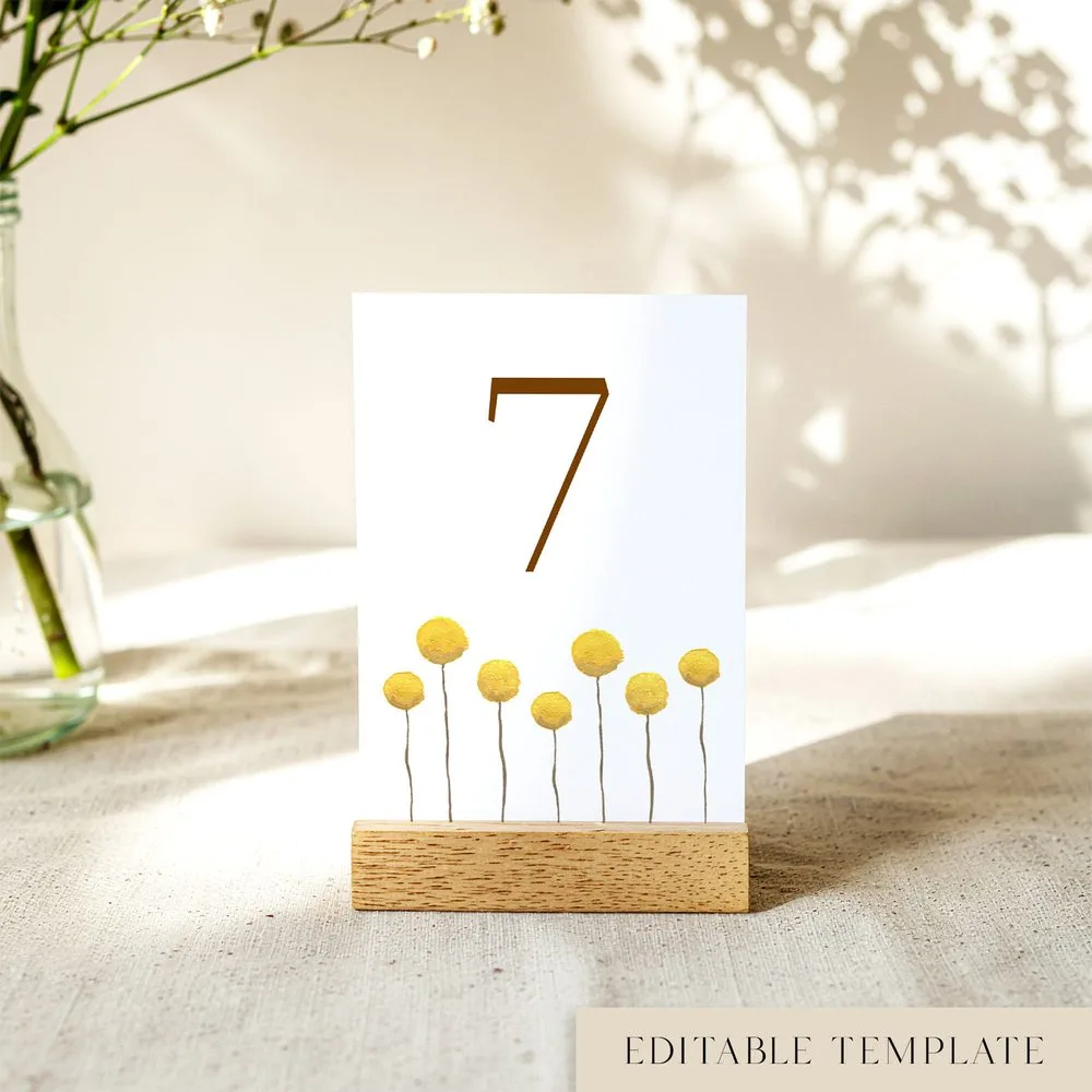 Minimalist wedding table number template with hand-painted billy buttons, shown in a wooden stand, fully editable in Canva.